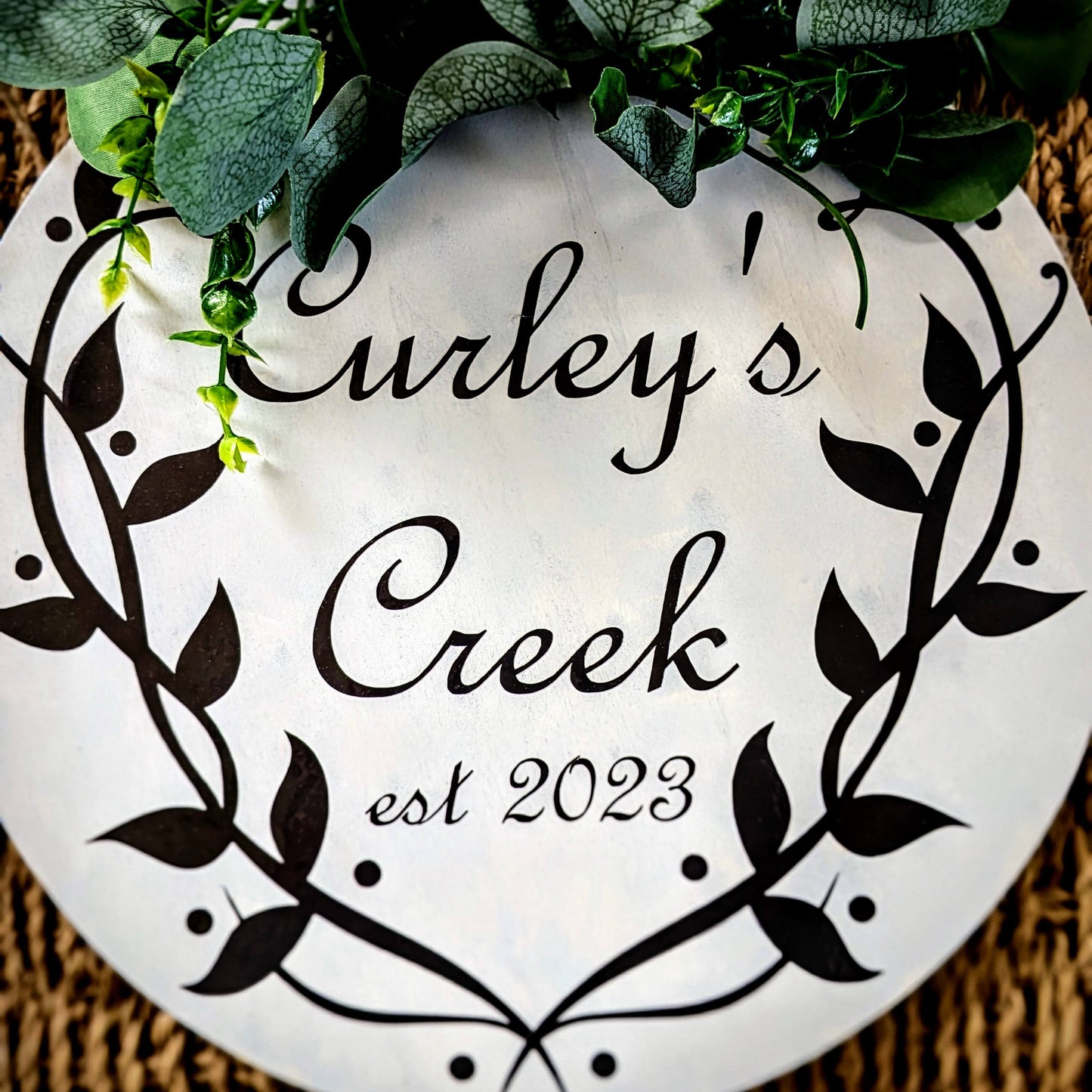 Decorative sign with 'Curley's Creek est 2023' text on a woven background